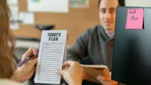 Two colleagues organizing tasks with a plan and sticky notes during a team meeting.