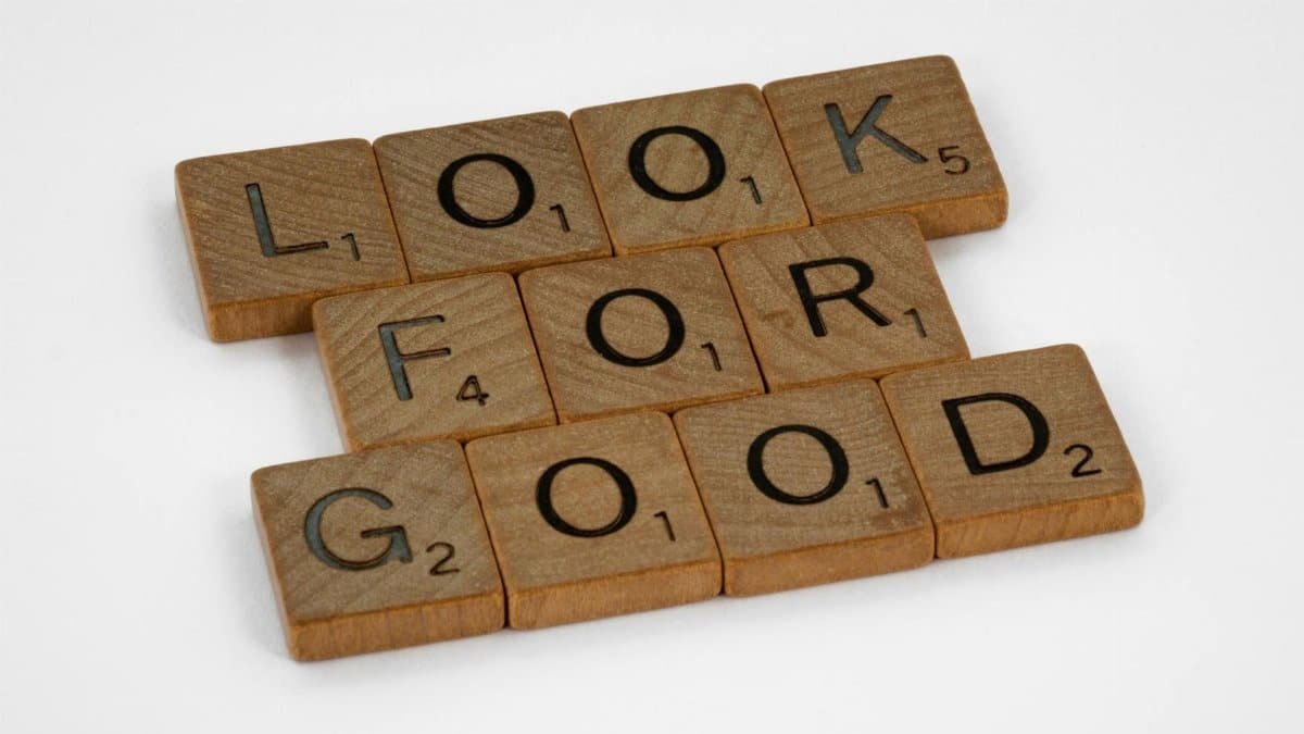 Close-up of wooden Scrabble tiles forming the phrase 'Look for Good' on a plain background.