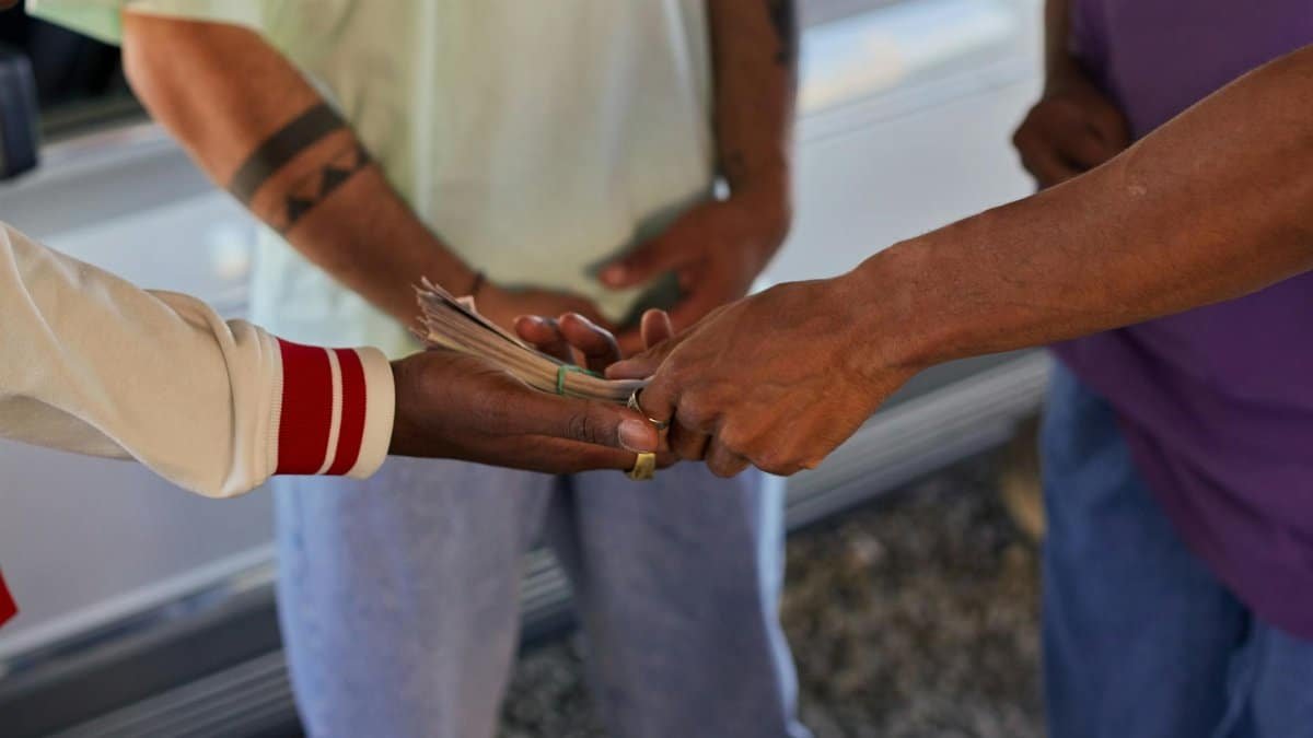 A close-up of hands exchanging paper money between two people outdoors.