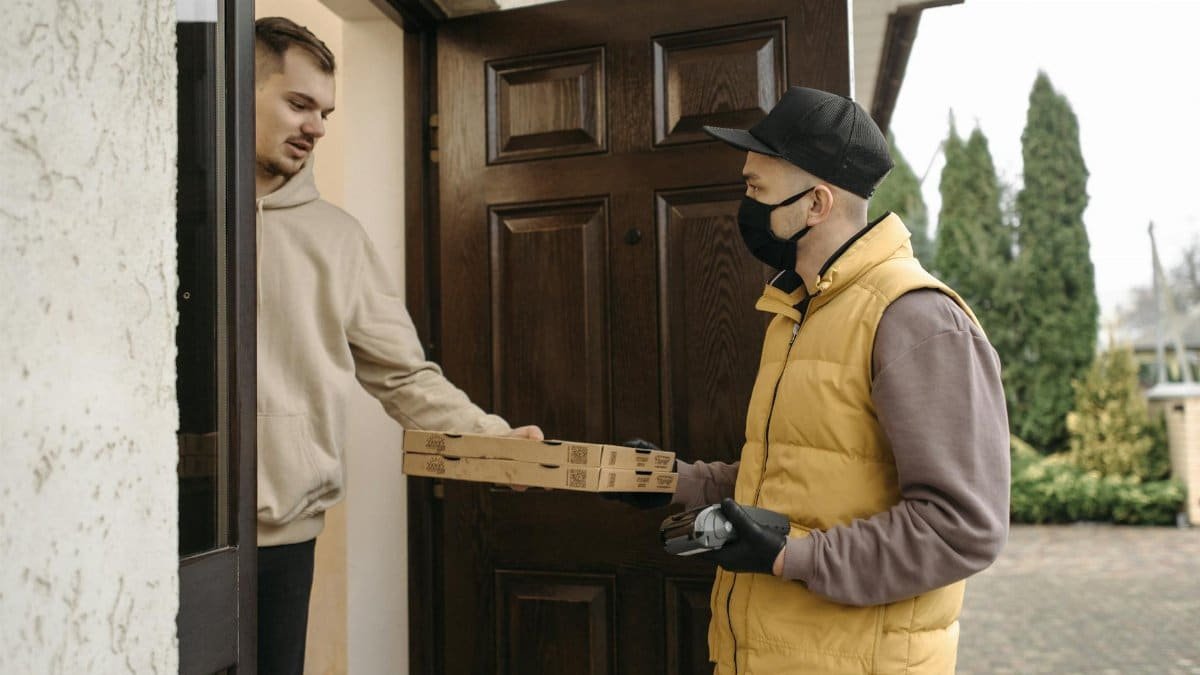 Courier delivering pizza boxes at the doorstep using contactless payment method.