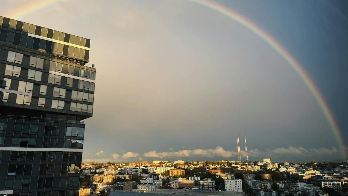 Vibrant rainbow arching over modern cityscape with high-rise building at dusk.