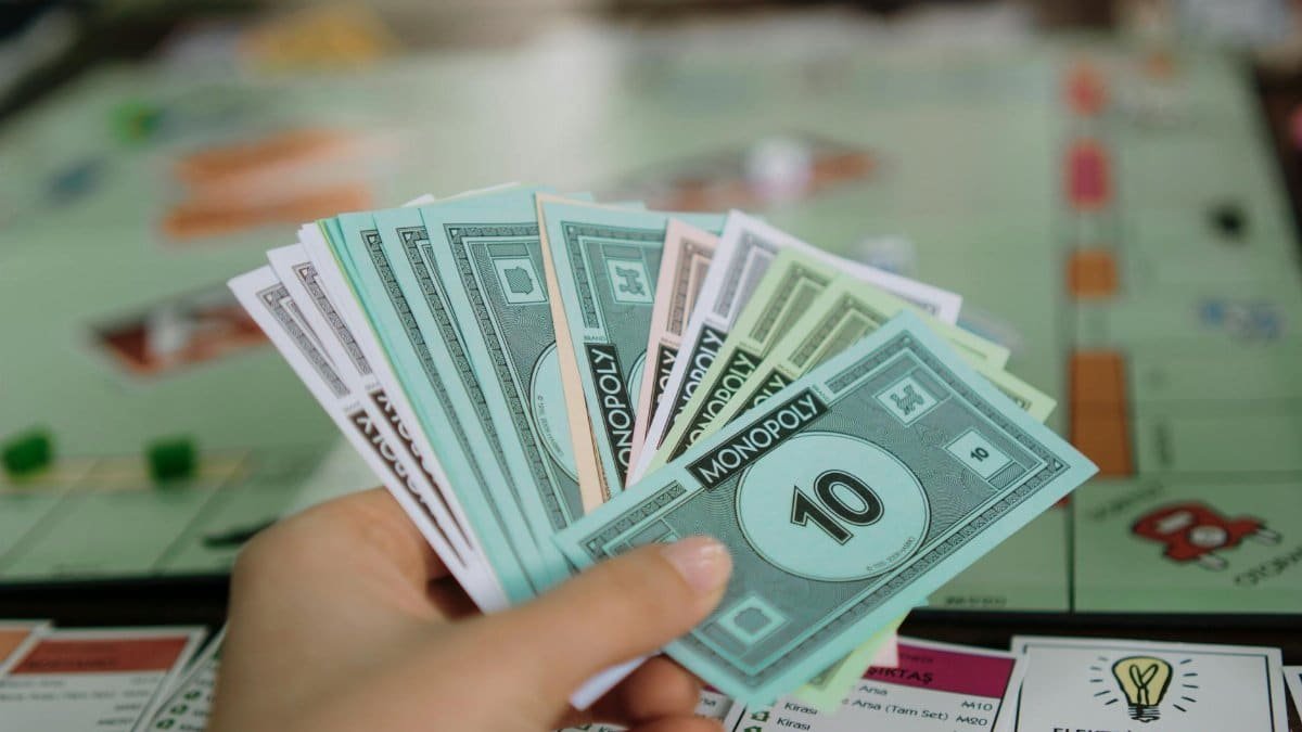 Close-up of a hand holding Monopoly money with board game in the background.