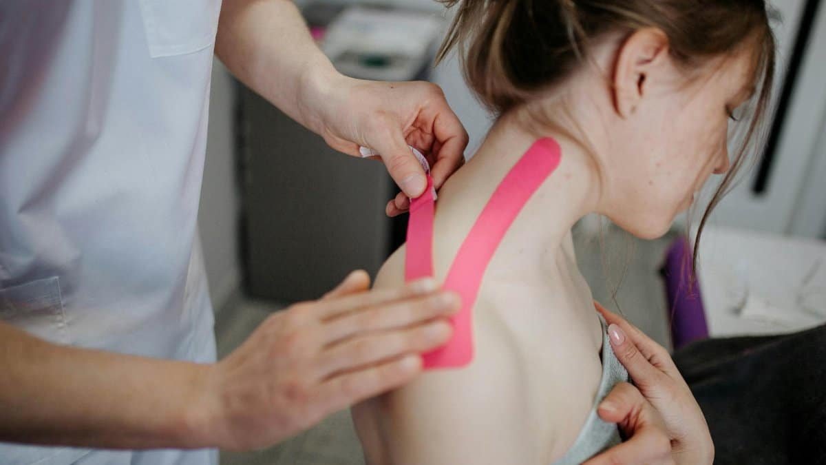 A physiotherapist applies kinesio tape to a woman's shoulder for pain relief and treatment.