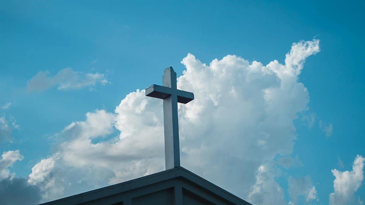 Low angle view of a cross on a church roof with a vibrant blue sky and clouds.