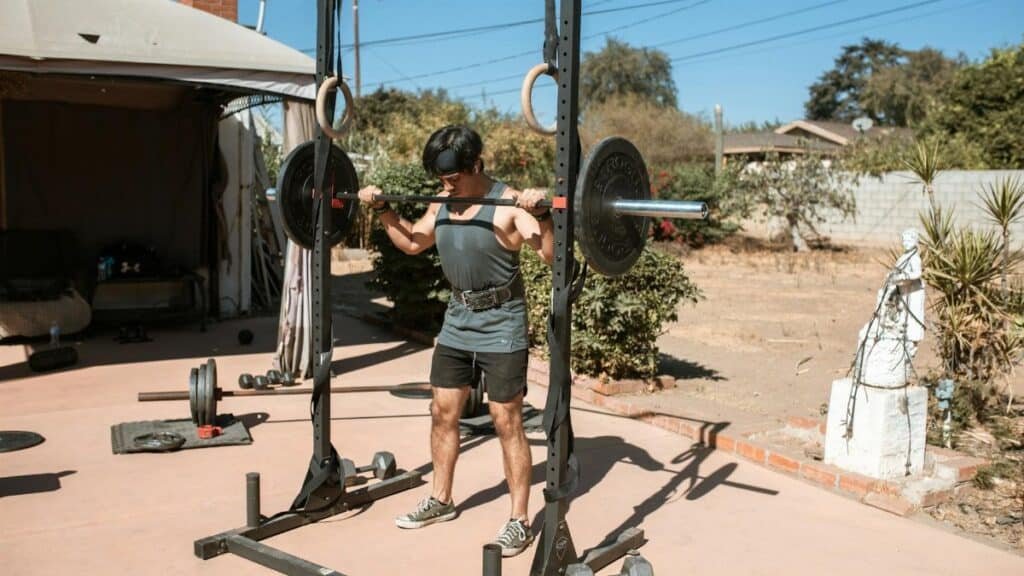 Man doing a barbell squat in an outdoor gym setting for strength training.