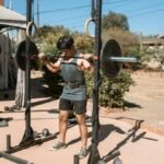 Man doing a barbell squat in an outdoor gym setting for strength training.