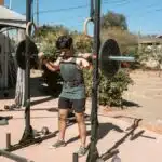 Man doing a barbell squat in an outdoor gym setting for strength training.