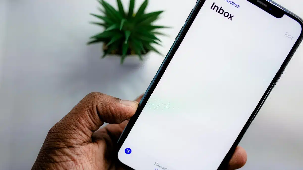 A close-up view of a smartphone screen displaying the email inbox, held by an adult's hand.