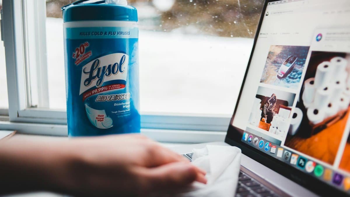 A person cleaning a laptop with Lysol disinfectant wipes by a window.