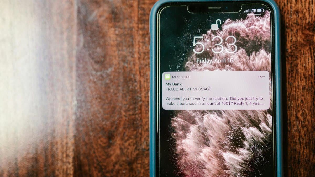 Close-up of a smartphone displaying a fraud alert notification on a wooden surface.