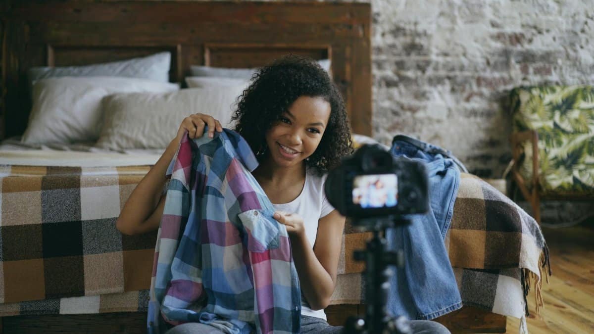 Young woman recording a clothing haul video in her cozy bedroom setting.