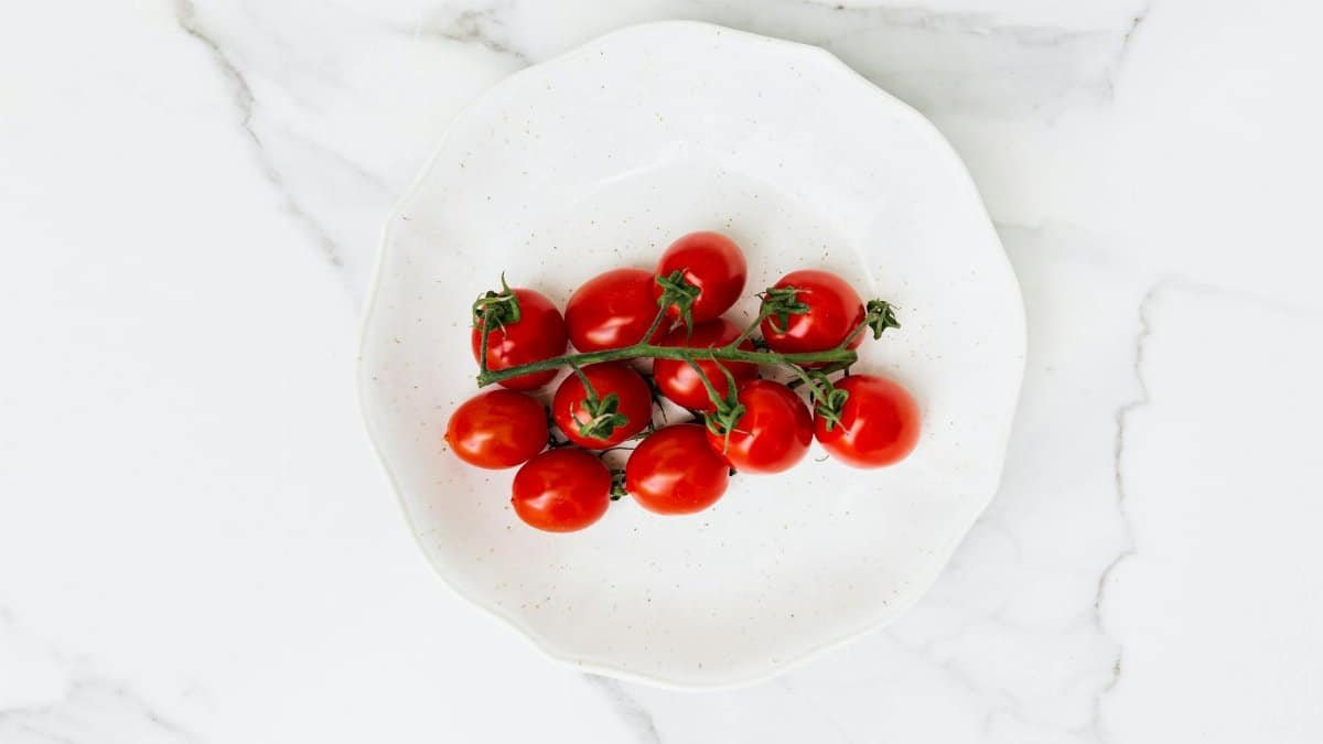 A close-up of fresh cherry tomatoes on a white ceramic plate, shot from above.