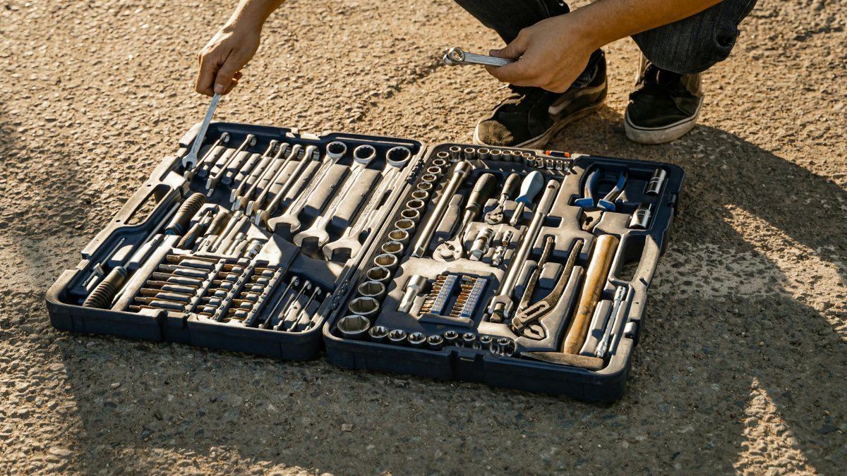 Mechanic organizing a toolkit outdoors on a sunny day, highlighting essential hand tools for repair and maintenance.