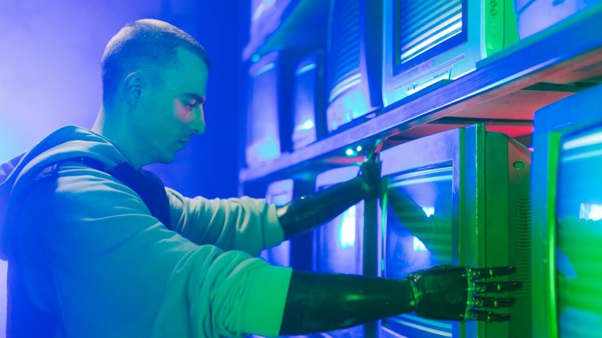 Man with prosthetic arms interacting with stack of CRT televisions, showcasing technology.