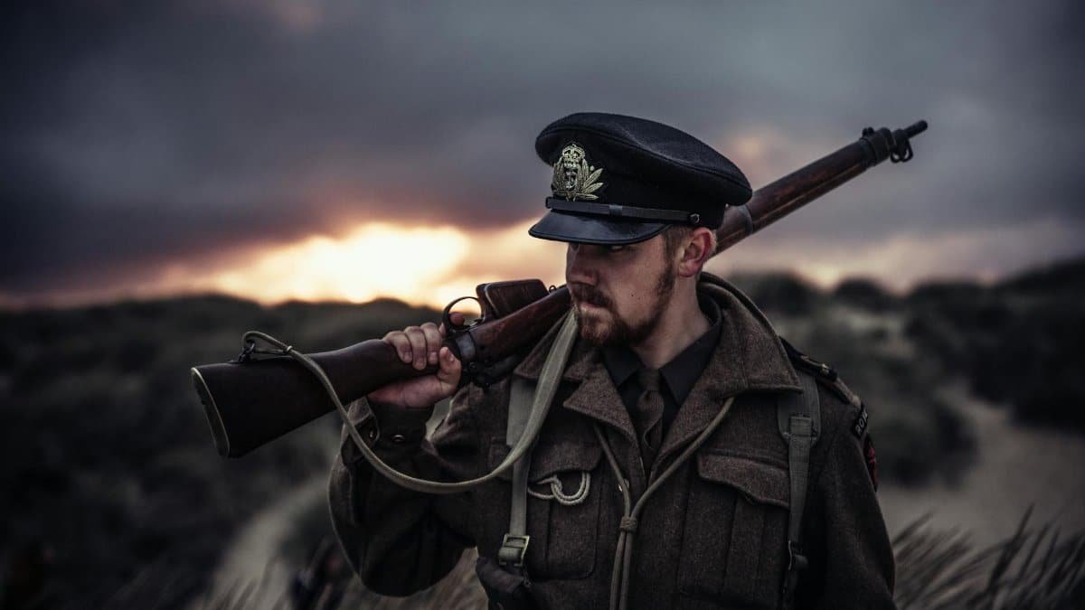 A soldier in uniform holding a rifle against a dramatic sunset background.