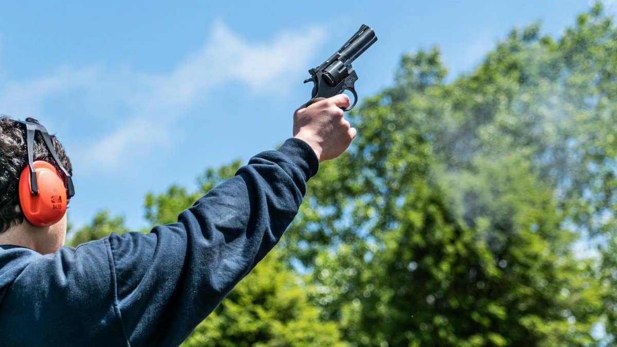 Close-up of a person firing a starting pistol outdoors with blue sky