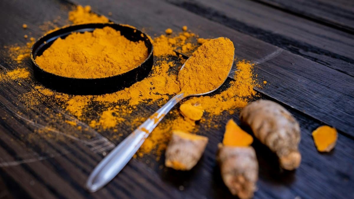 Vibrant turmeric powder and root on a dark wooden surface, emphasizing natural spices.