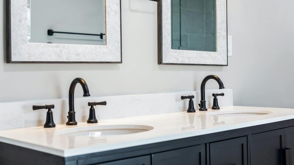 Sleek bathroom vanity featuring a double sink setup with stylish black faucets and framed mirrors.