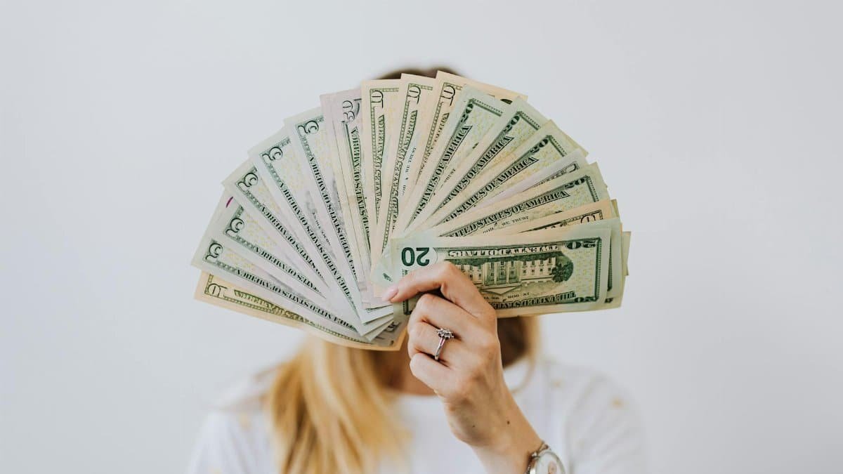 Close-up of a person holding a fan of US dollar bills on a neutral background.