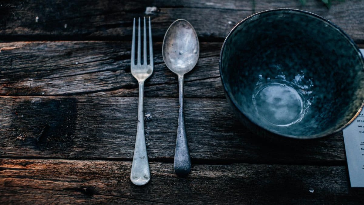 High angle of round shaped bowl near fork and spoon on rough wooden table in daytime