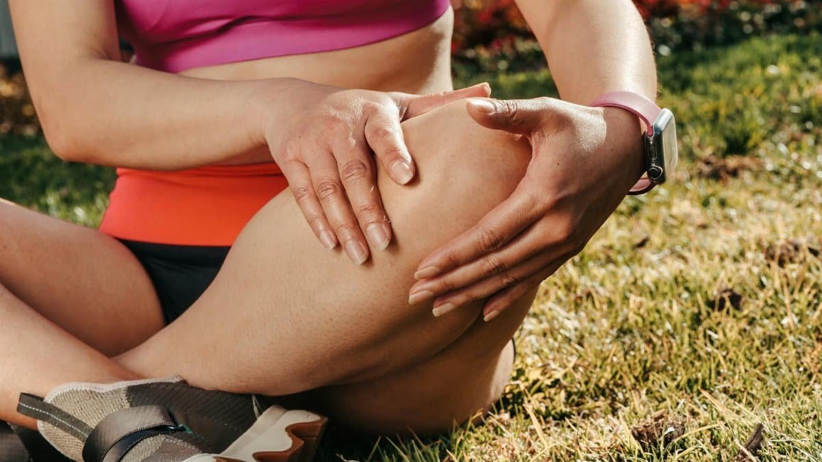 Close-up of a woman sitting cross-legged on grass, holding her knee, wearing a smartwatch.