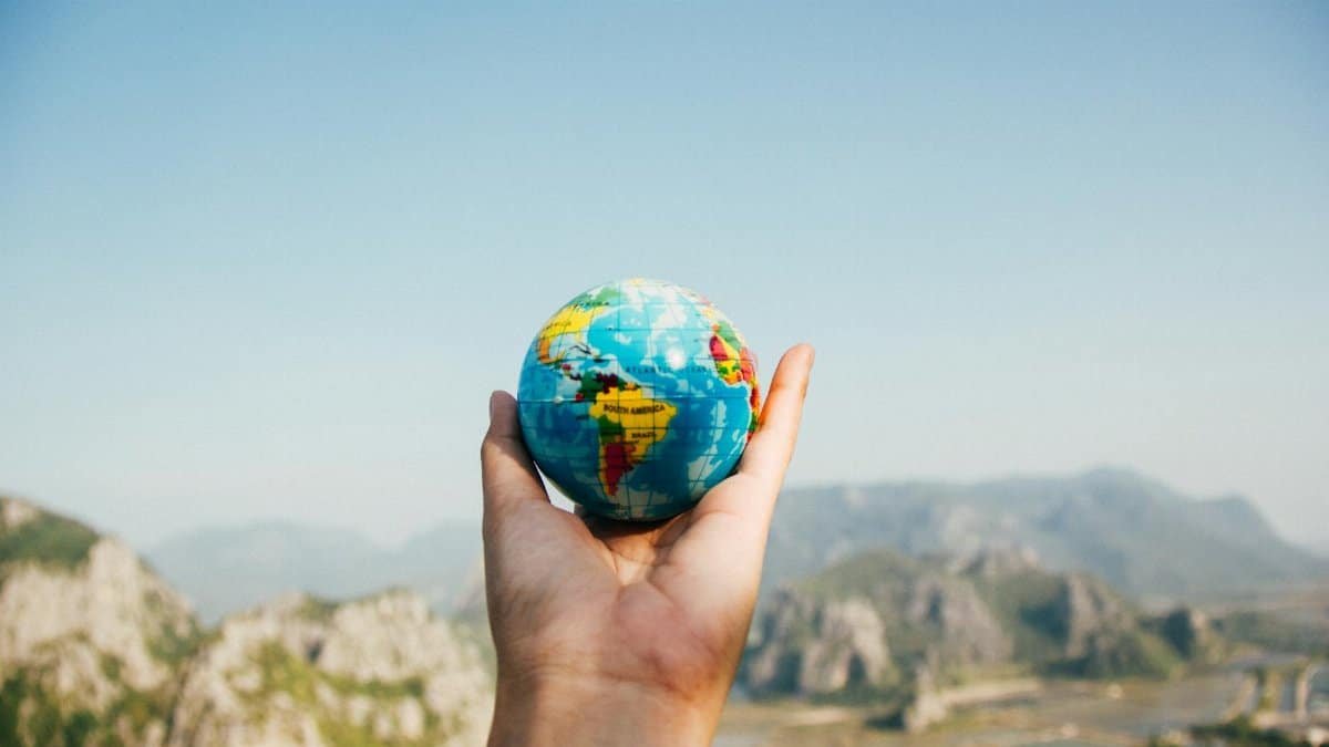 Hand holding a globe against a mountain background symbolizing travel and exploration.