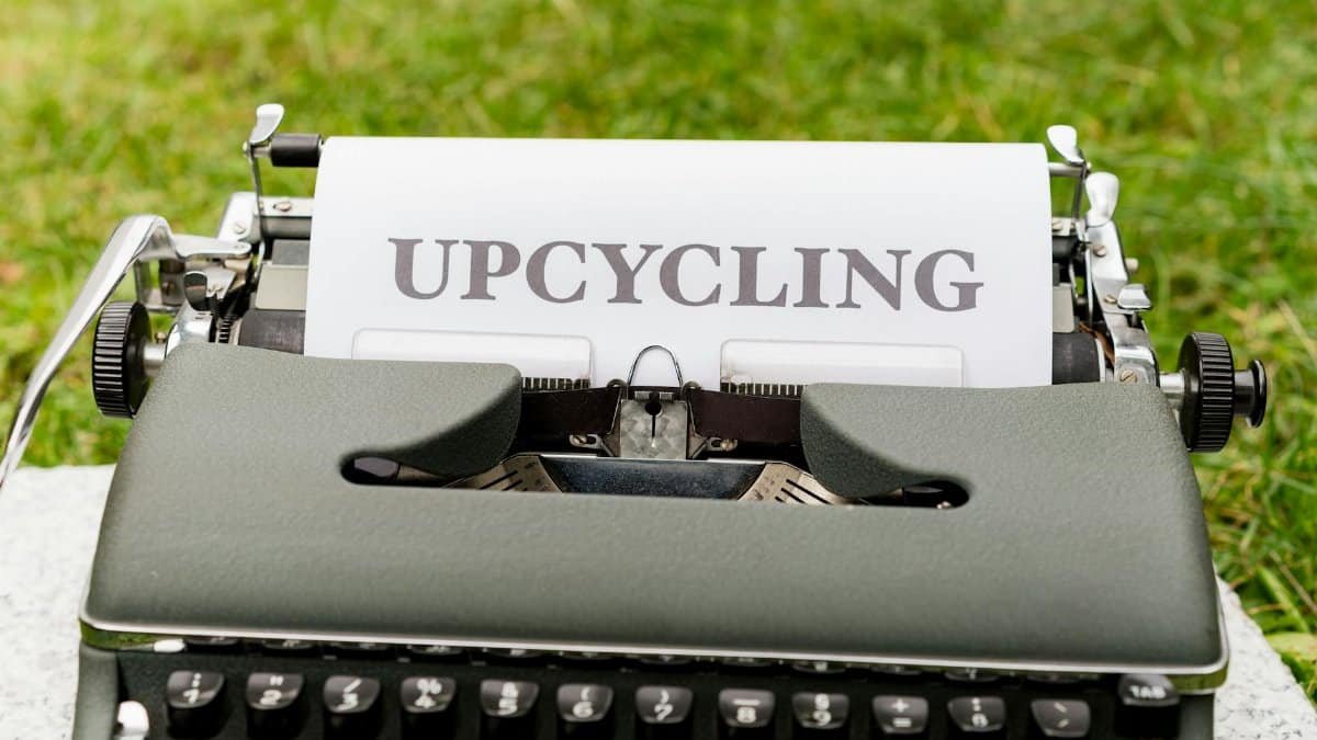 A retro typewriter displaying the word 'upcycling' outdoors on grassy ground.