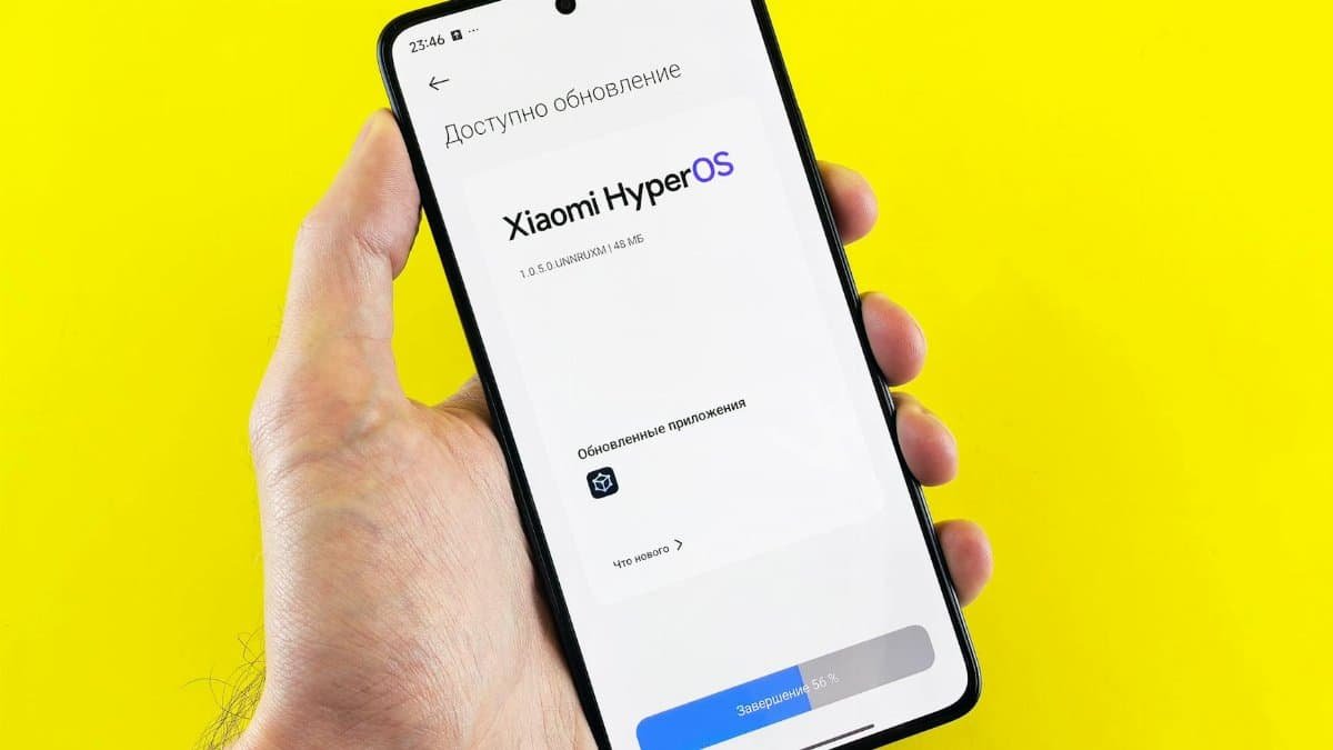 Hand holding smartphone showing Xiaomi HyperOS update screen on yellow background.