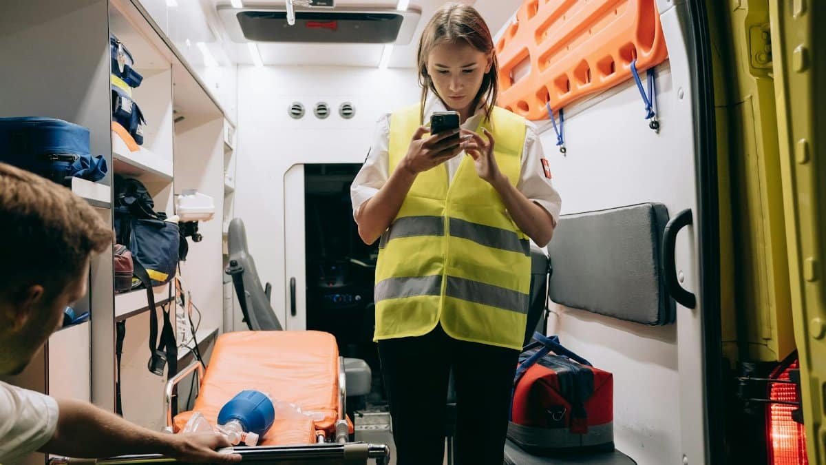 Female paramedic using smartphone inside an ambulance preparing for emergency response.