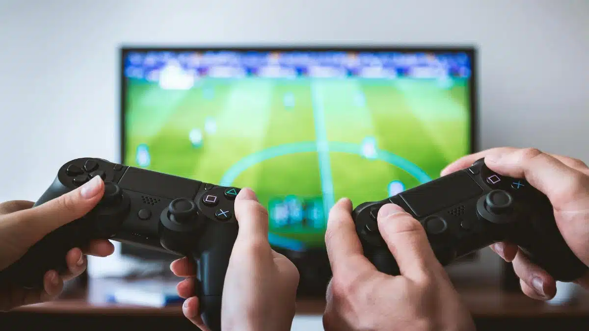 Close-up of hands holding gaming controllers in front of a TV. Engaged in a video gaming session.