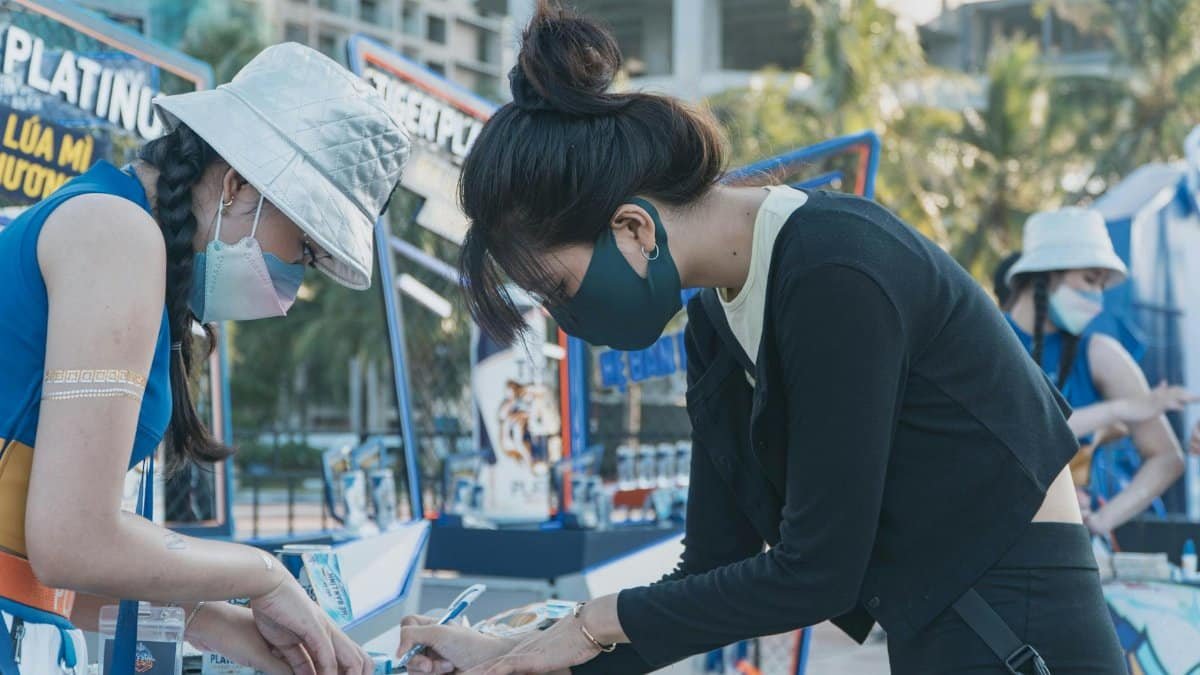 Two young women in masks volunteering outdoors, filling out forms at an event table.