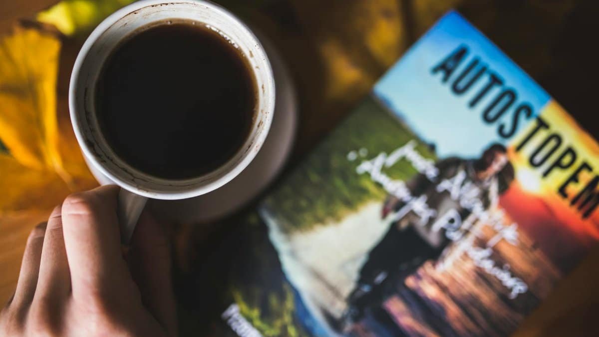 A warm cup of coffee beside a travel book on an autumn-themed surface.