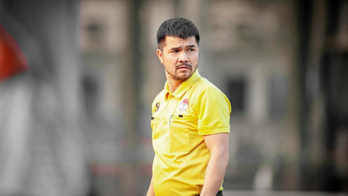Focused soccer coach wearing yellow shirt during outdoor training session in Hanoi, Vietnam.