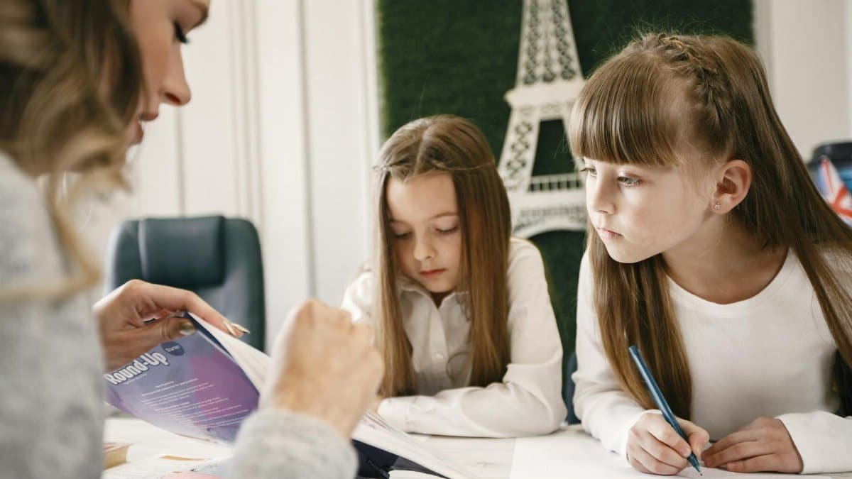 Two girls attentively studying with a tutor in a classroom setting.