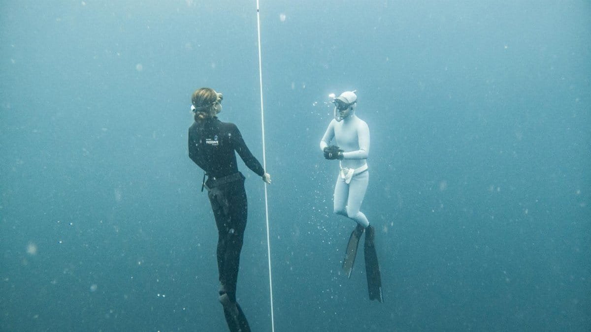 Two freedivers explore deep blue waters in Lombok, Indonesia, using guide rope for orientation.