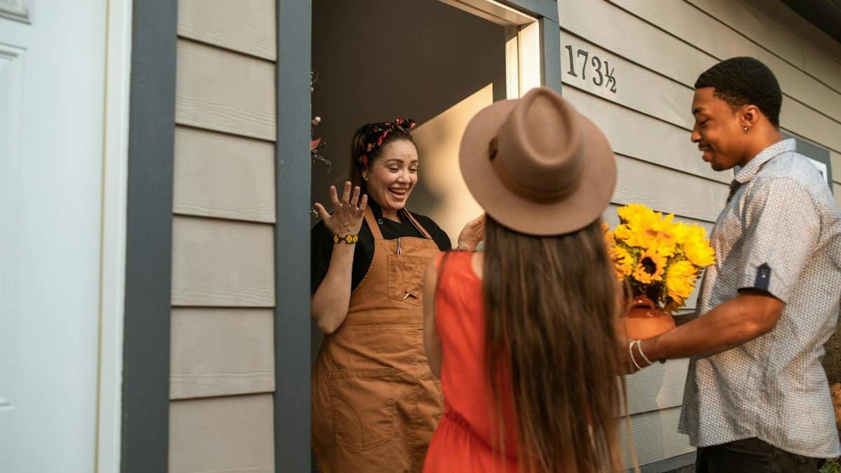 Friends surprising a hostess with sunflowers at the doorway, sharing smiles and joy.