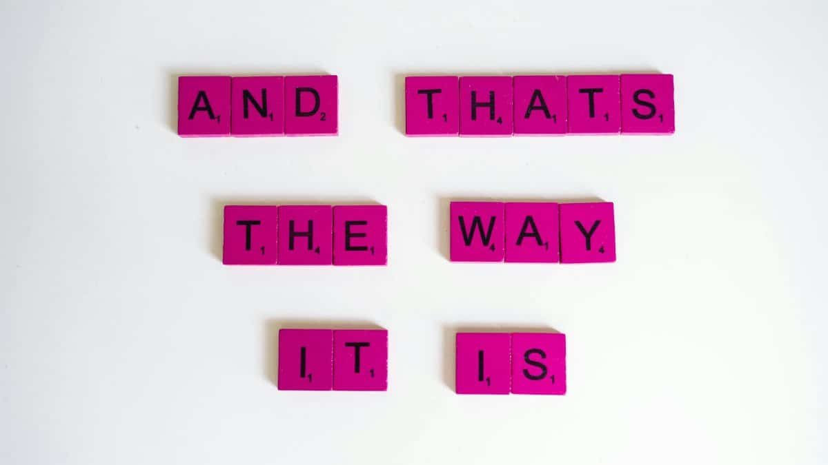Inspirational quote 'And That's The Way It Is' on pink Scrabble tiles.