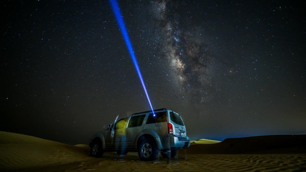 An SUV parked in the desert under a starry night sky with the Milky Way visible.