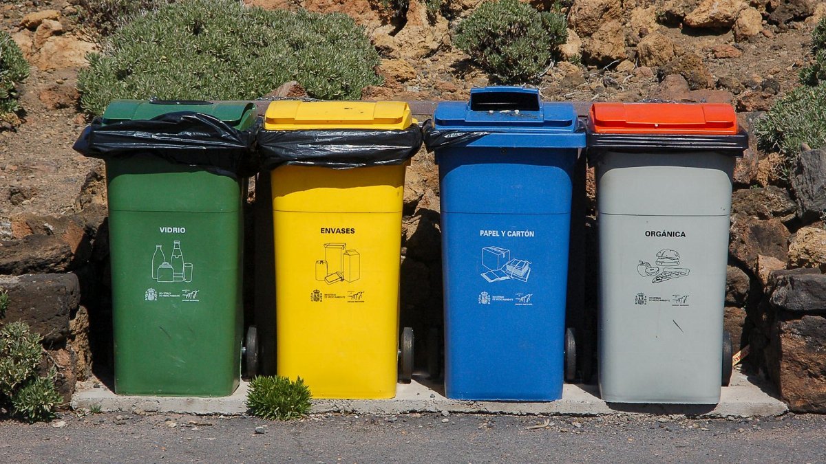 Four recycling bins for glass, packaging, paper, and organic waste outdoors.