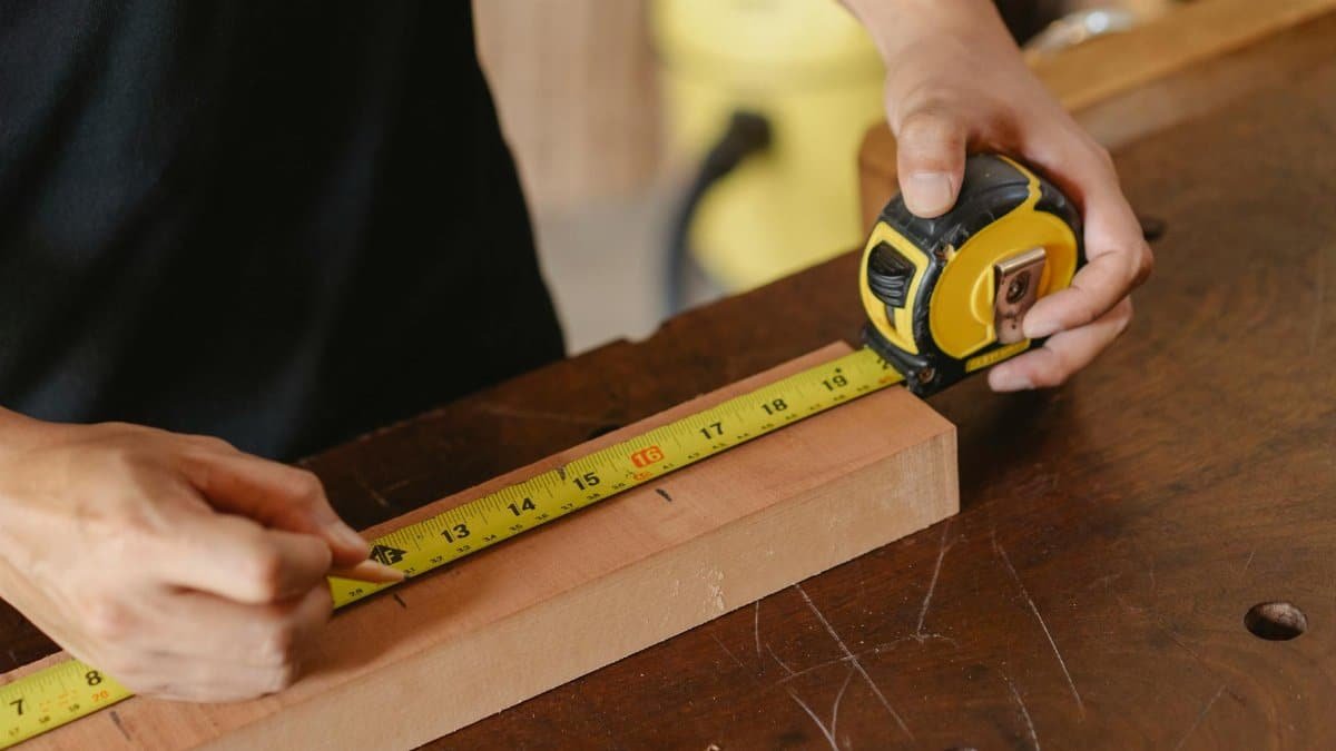 Close-up of a carpenter measuring a wooden plank with a tape measure on a workbench.
