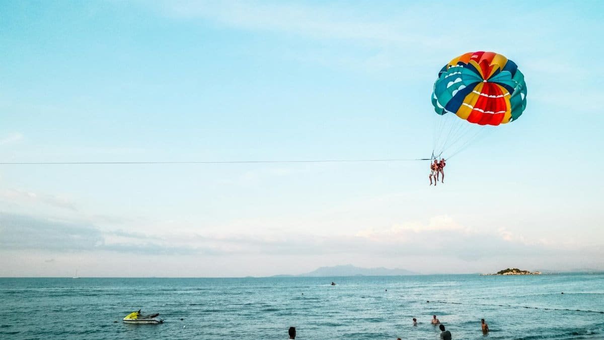 Exciting parasailing experience over the ocean with a vibrant parachute and scenic beach view.