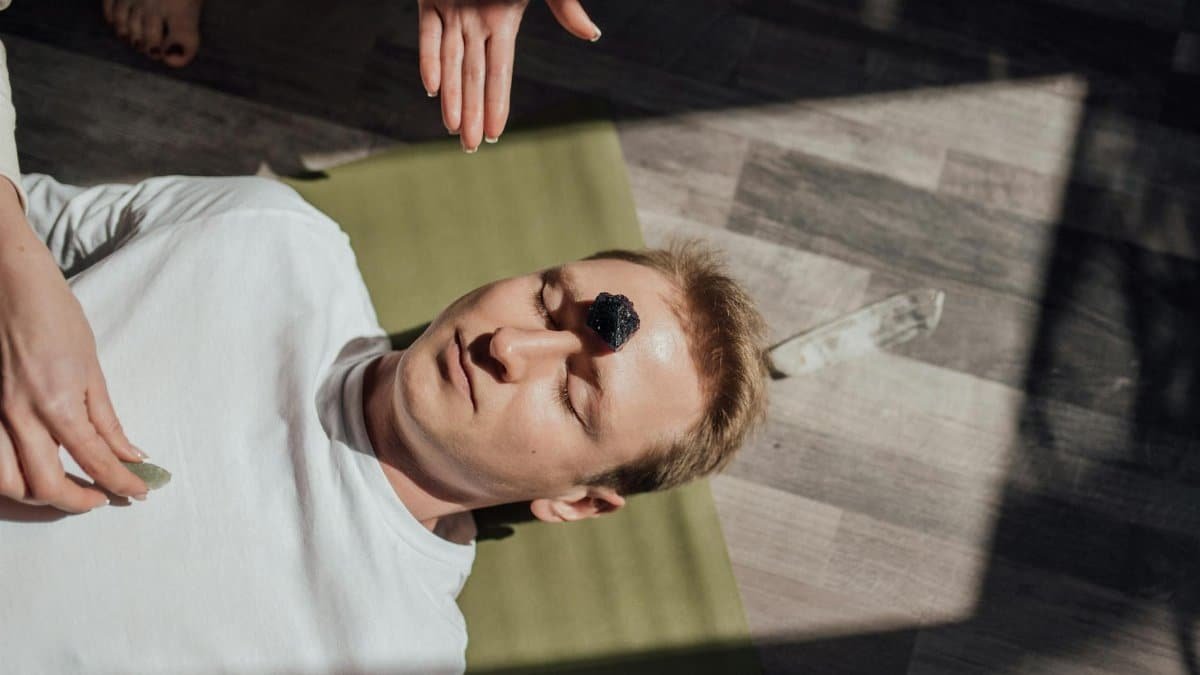 Man lying down with healing crystals for a relaxation therapy session indoors.