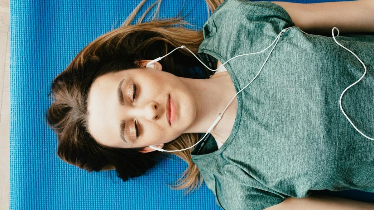 Young woman meditating with closed eyes on a yoga mat, listening to music.
