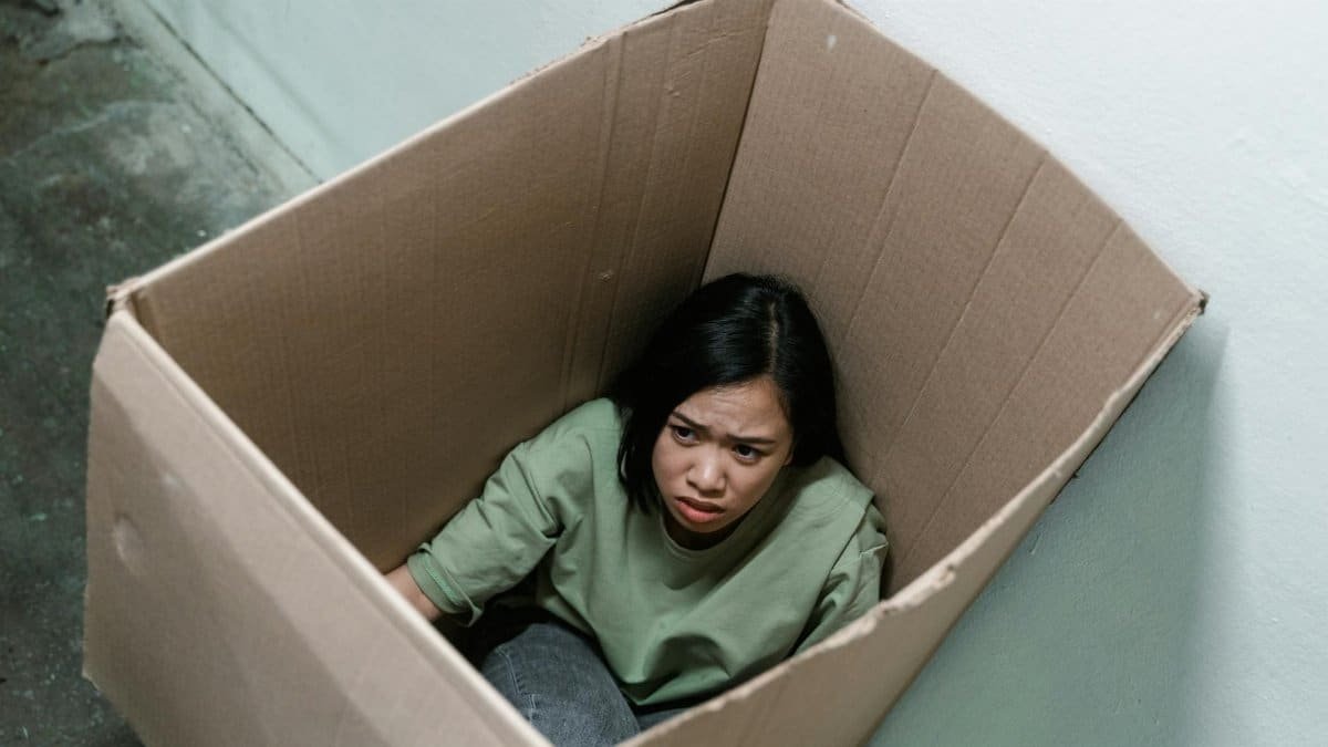 Woman in a cardboard box, symbolizing feelings of anxiety and claustrophobia.