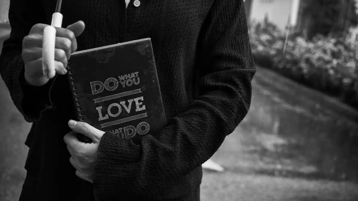 Close-up black and white image of a person holding a motivational notebook outdoors.
