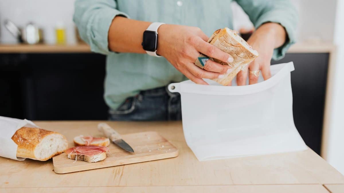 A person packs a sandwich into a silicone bag on a kitchen counter, highlighting eco-friendly food storage.