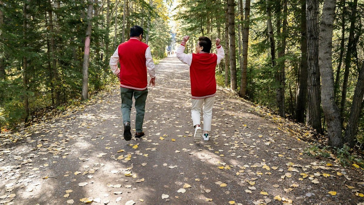 A couple enjoying a walk on a leaf-covered path in a lush forest during autumn.