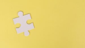 Simple white jigsaw puzzle piece placed on a bright yellow background with ample copy space.