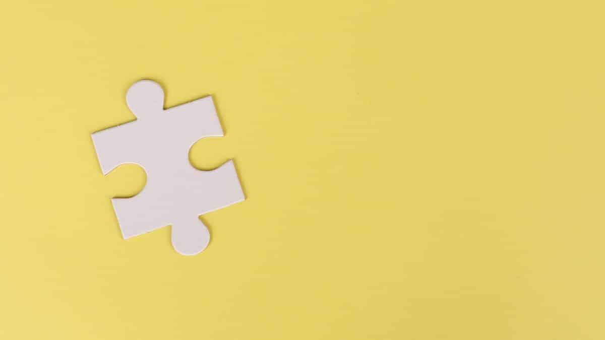 Simple white jigsaw puzzle piece placed on a bright yellow background with ample copy space.