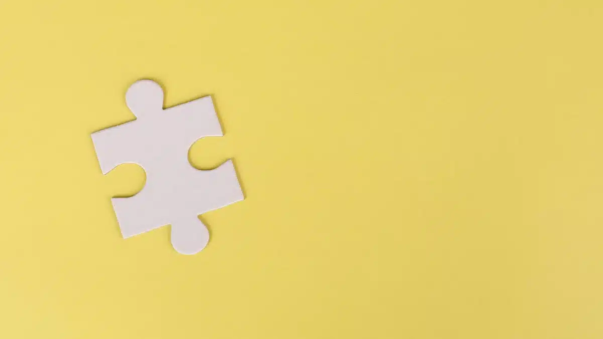 Simple white jigsaw puzzle piece placed on a bright yellow background with ample copy space.